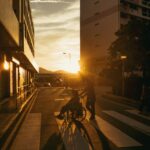 A person pushing a wheelchair along a quiet street at sunset in Singapore, capturing the quiet weight of caregiving.
