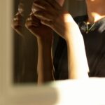A person holds a ceramic cup close to their face in warm dramatic light, eyes partially visible, capturing the quiet inward experience of living with anxiety that feels like personality.