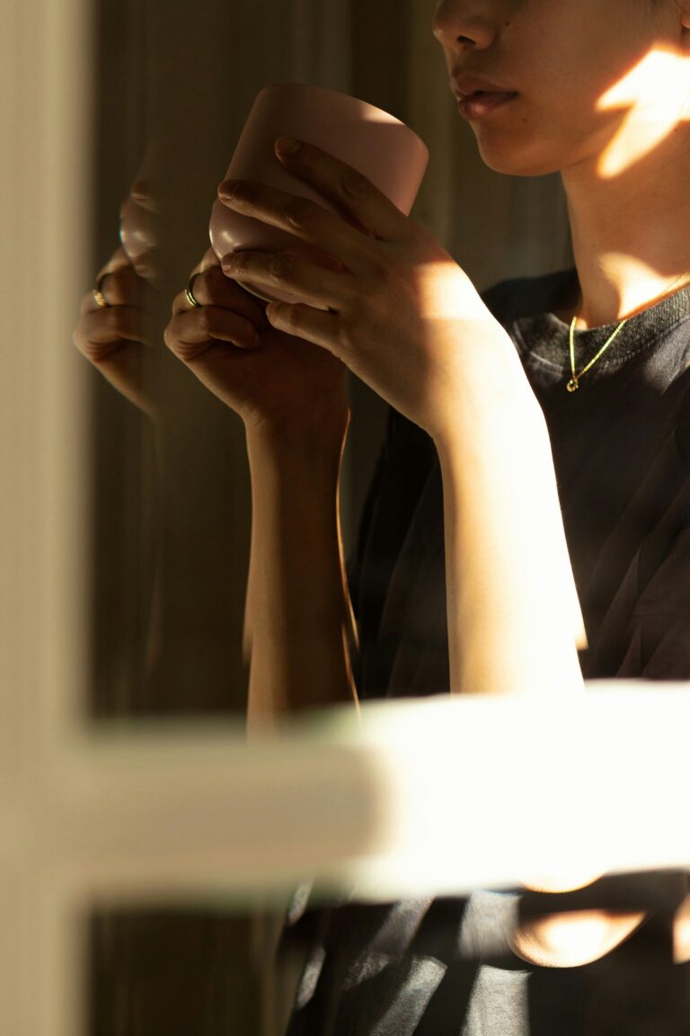 A person holds a ceramic cup close to their face in warm dramatic light, eyes partially visible, capturing the quiet inward experience of living with anxiety that feels like personality.