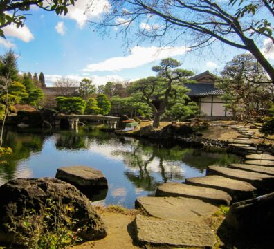 Stepping stones cross a still pond in a Japanese garden, evoking the quiet, deliberate process of grounding and finding your way back to calm.
