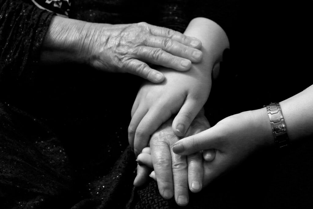 Different generations of hands rest together, an elderly person's hands over a younger adult's hands, quietly capturing the experience of the sandwich generation holding both the older and younger generation at once.