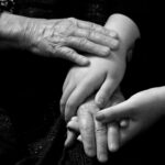 Different generations of hands rest together, an elderly person's hands over a younger adult's hands, quietly capturing the experience of the sandwich generation holding both the older and younger generation at once.