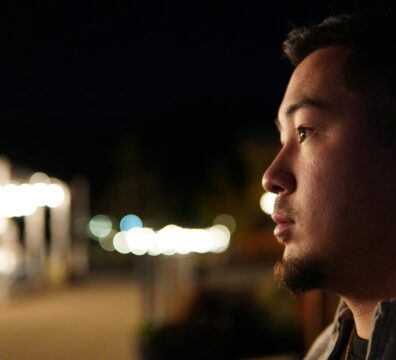 A man alone at night gazes quietly into the distance, his face softly lit against a backdrop of blurred city lights, capturing the experience of carrying something privately while appearing composed to the world.