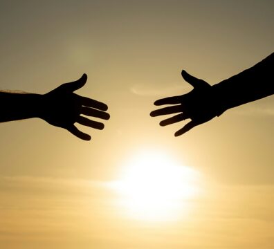 Two hands reach toward each other in silhouette against a warm golden sunset, with a gap between them that evokes the longing for connection and the distance that attachment patterns can create.